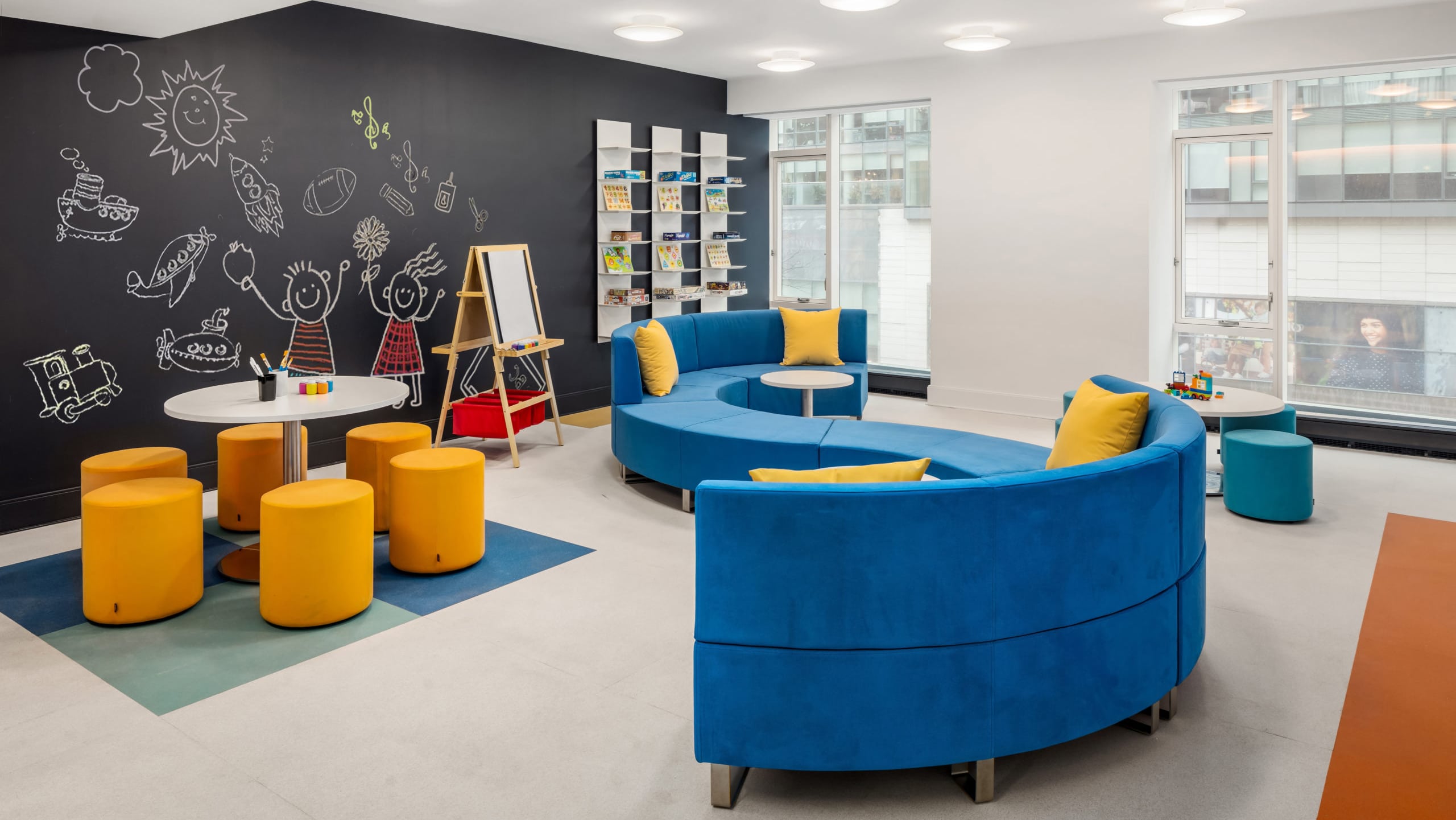 Kid's playroom at The Hayworth condos in NYC. A large "S" shaped couch, art supplies, and a black accent wall with a mural.