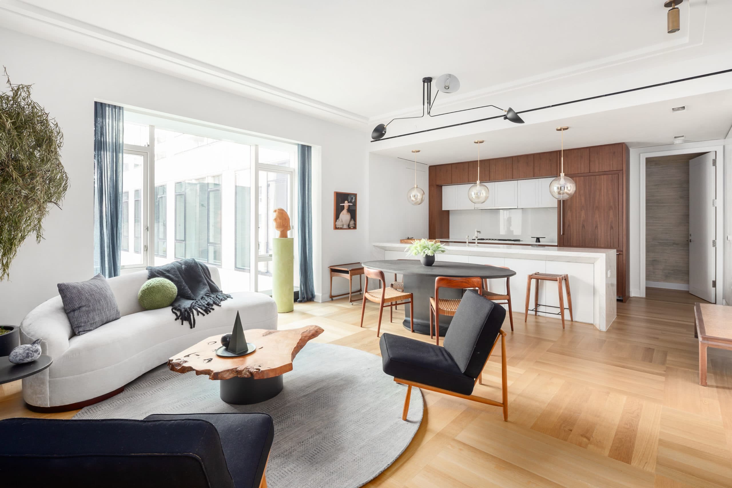 Open concept condo interior at The Hayworth in New York. Living room with furniture and kitchen with island & wood cabinets.