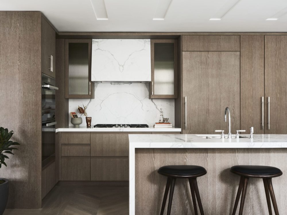 Kitchen at 40 Bleecker St condos in New York City. Center island, white marble countertops and natural wood kitchen cabinets.