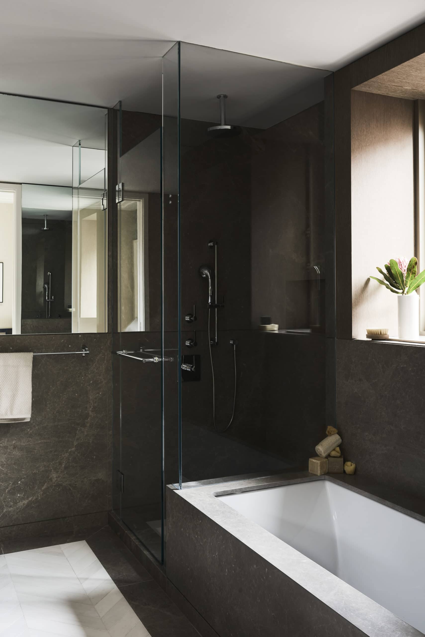 Bathroom at 40 Bleecker St residences in New York. Glass standing shower, soaking tub, and black stone walls with veining.